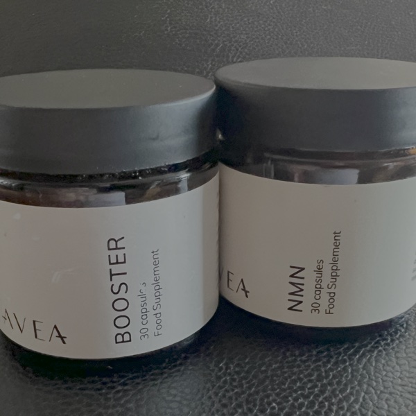 Two AVEA supplement jars side by side — Booster and NMN, 30 capsules each, dark grey lids on frosted glass