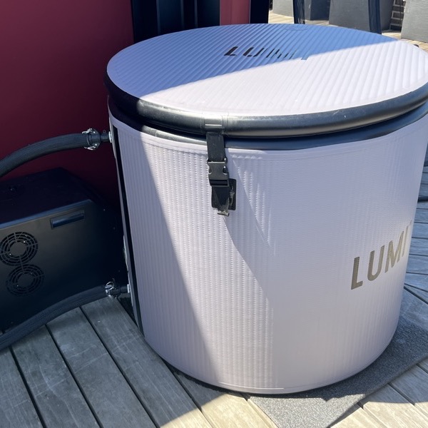 LUMI Pod Pro cold plunge on a deck, white textured barrel with black rim, hose connected to the Mini Chiller 2 unit beside it